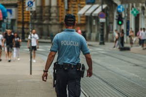 A police officer walking down a city street during the day, maintaining law and order.